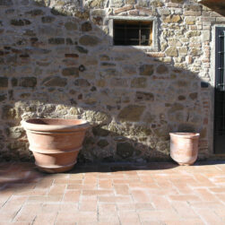 Fioriera a Parete Liscia in Terracotta di Impruneta con piedi smerlati integrati per un corretto deflusso dell’acqua, decorata con piante rampicanti colorate.