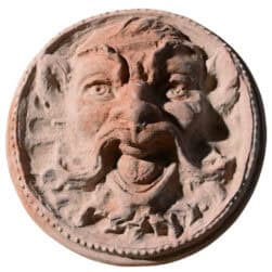 Mascherone circolare in terracotta con volto espressivo scolpito in rilievo decorativo