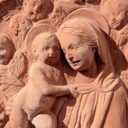 "Madonna with Child and Six Angels" in terracotta, inspired by the Della Robbia workshop, with a corded frame, symbolizing serenity and sacred harmony.