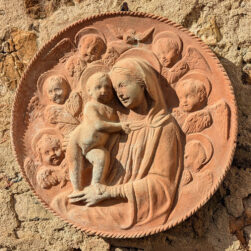 "Madonna with Child and Six Angels" in terracotta, inspired by the Della Robbia workshop, with a corded frame, symbolizing serenity and sacred harmony.